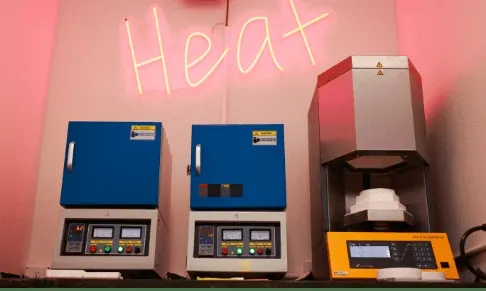 Three ceramic furnaces in the lab under a neon Heat sign.