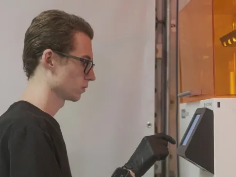 A lab technician in black scrubs loading one of the lab's 3D printers.