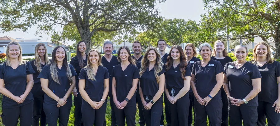 The Ocean Oaks Dental Group team outdoors under an oak tree, in navy scrubs.