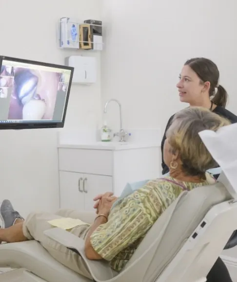 A patient in the chair looking at an enlarged image of her teeth on the wall screen while her dentist explains.
