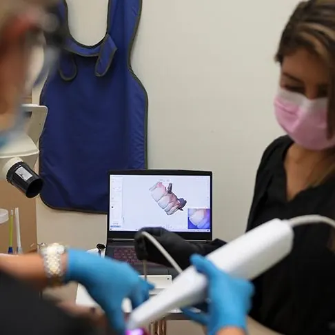 An intraoral scanner capturing a digital impression, shown on a laptop.