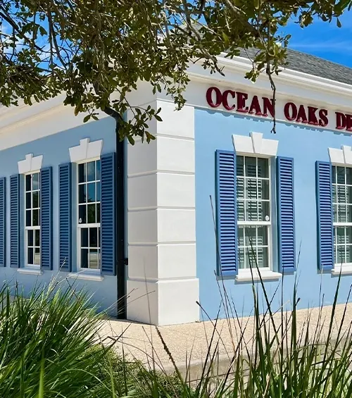The Ocean Oaks Dental Group building on 37th Place, blue shutters and white columns under the oaks.