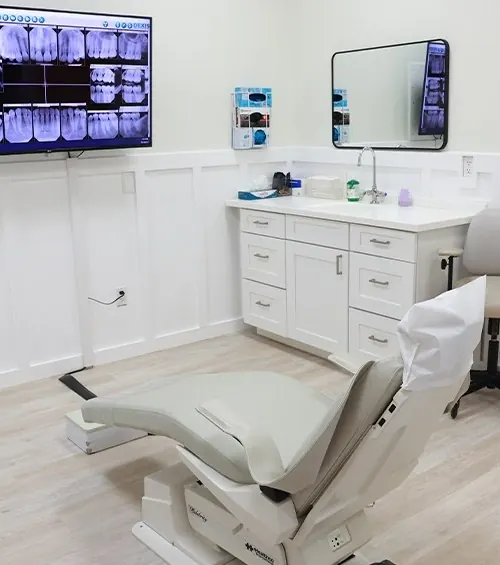 A treatment room: white wainscoting, a dental chair and x-rays on the wall screen.